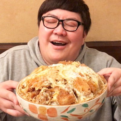 大盛りのカツ丼を両手で抱え、満面の笑みを浮かべる男性。