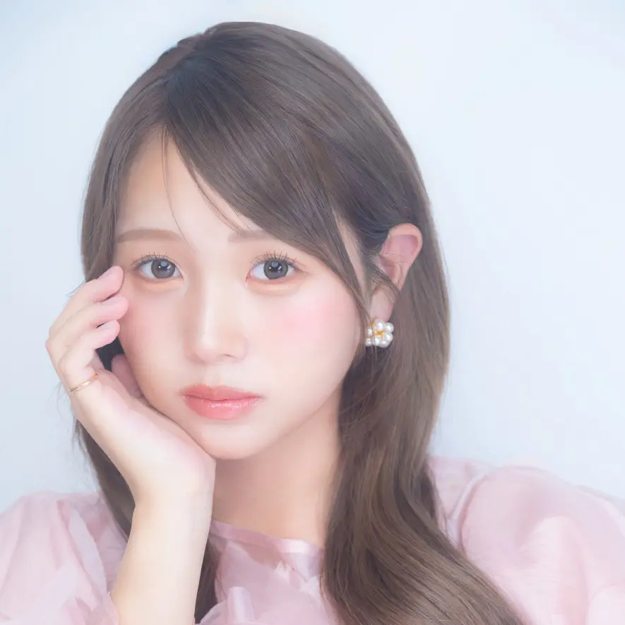 ライトブラウンの髪の若いアジア人女性が、ピンクの服を着て頬に手を添えているポートレートです。
