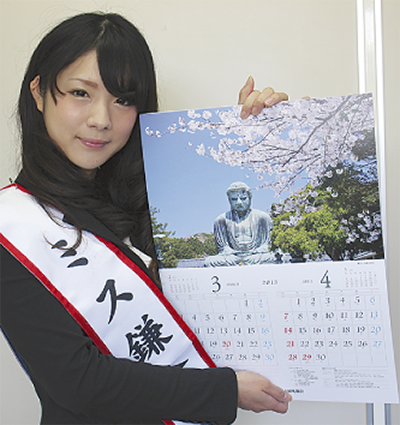 「ミス鎌倉」のたすきをかけた若い女性が、鎌倉大仏と桜が写ったカレンダーを持っている画像です。