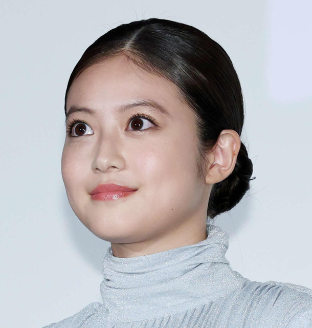 水色のタートルネックの服を着た若い日本人女性が、髪を後ろでまとめて、少し上を見上げている顔のクローズアップ画像です。