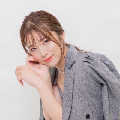 グレーのジャケットを羽織り、頬杖をついて微笑む女性の画像です。