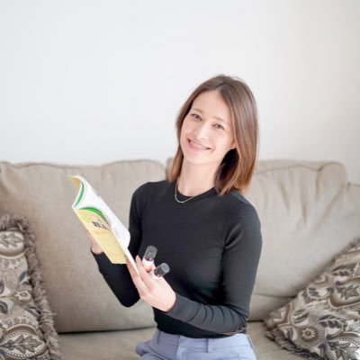 ソファに座り、アロマの本と商品を手に持ちながら微笑む箕輪三香さん。