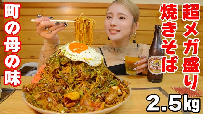 金髪の女性（ますぶちさちよさん）が、2.5kgの超メガ盛り焼きそばと瓶ビールを前に、笑顔で麺を箸で持ち上げている画像。