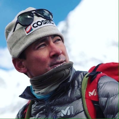 雪山を背景に、帽子をかぶりサングラスをかけた登山家風の日本人男性が上を見上げています。
