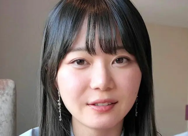 雨が降る窓の外を、憂いを帯びた表情で見つめる日本人女性。窓ガラスには雨粒がつき、ぼやけた街の光が反射しています。彼女の横顔からは、内省的な雰囲気と繊細さが感じられます。