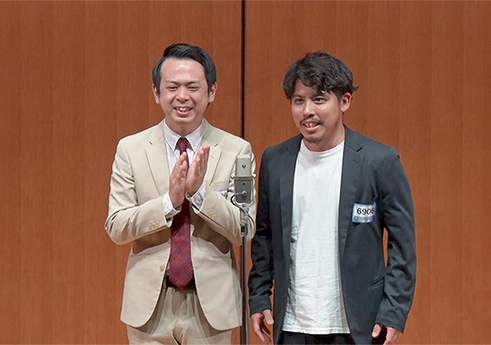 スーツを着た男性と座って話している男性の、お笑いコンビの舞台の様子