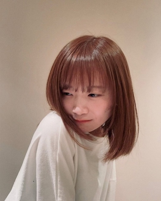 「白いTシャツを着て少し首を傾け、はにかんだ表情で横を見る秋元真夏さん」