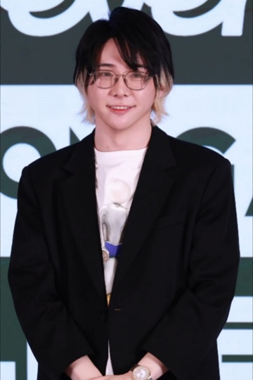 Mrs. GREEN APPLEの大森元貴さんが、黒いジャケットと眼鏡を着用して微笑んでいる上半身の写真です。