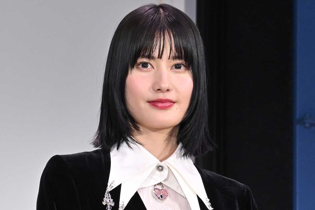 黒い上着と白い襟の服を着た、おかっぱ頭の若い女性がカメラ目線で微笑んでいるポートレート。