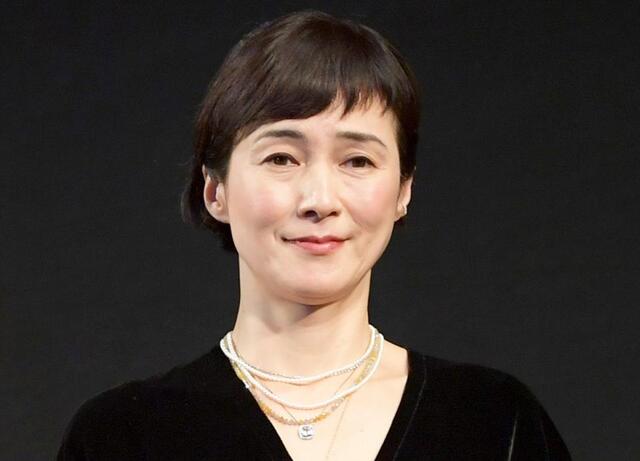 黒い服を着て、複数のネックレスを身につけた安田成美さんのポートレートです。髪型はショートで、穏やかな表情をしています。