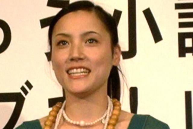 笑顔でカメラを見つめる、黒い髪を後ろでまとめた日本人女性のアップ写真。