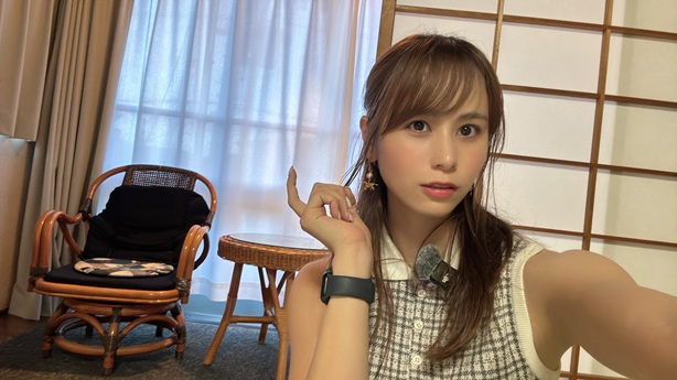 和室風の部屋で、籐製の椅子とテーブルを背景に自撮りをする女性の画像。女性はカメラに視線を向けています。
