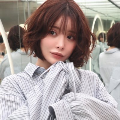明るい茶色のショートボブヘアで、ストライプのシャツを着た若い日本人女性のポートレート。優しい笑顔でカメラを見つめている。
