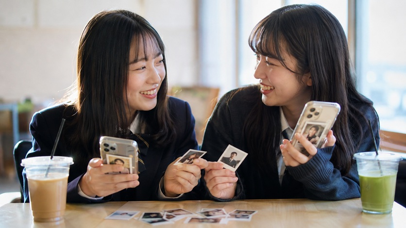 友達同士で証明写真を見せ合いスマホケースに入れて楽しむ様子